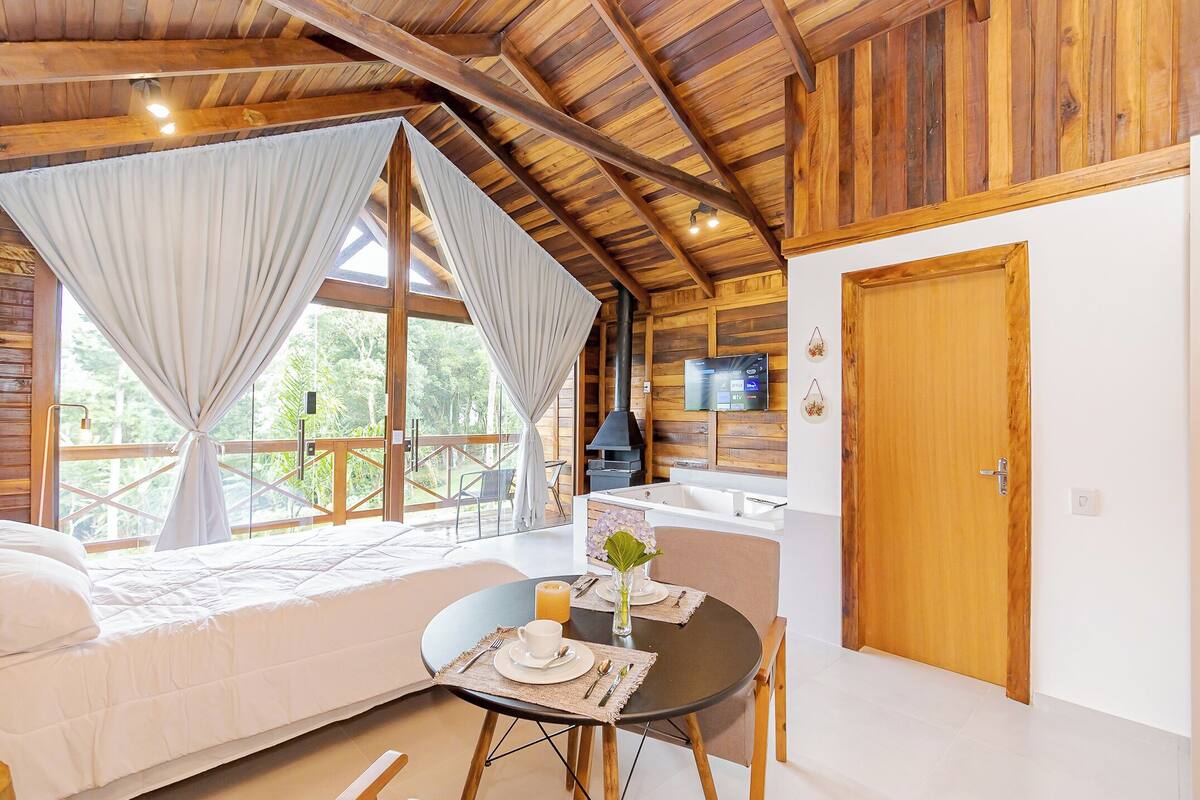 A cozy cabin with a bed, a dining table with a vase of flowers, and a view of the outdoors.
