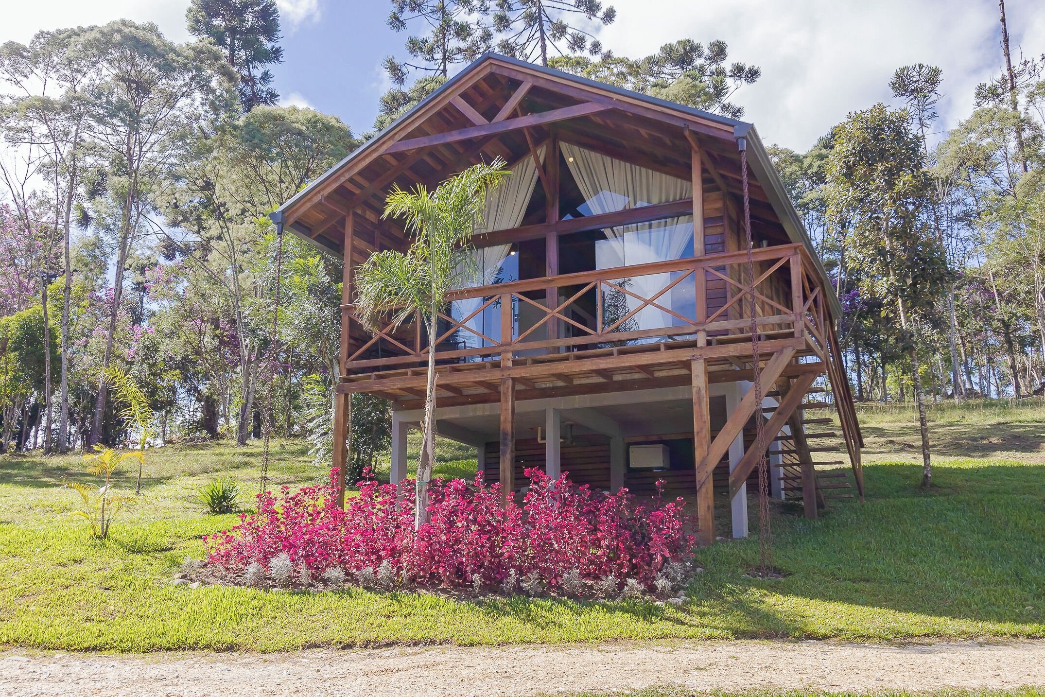 A wooden cabin with a balcony, surrounded by greenery and trees.