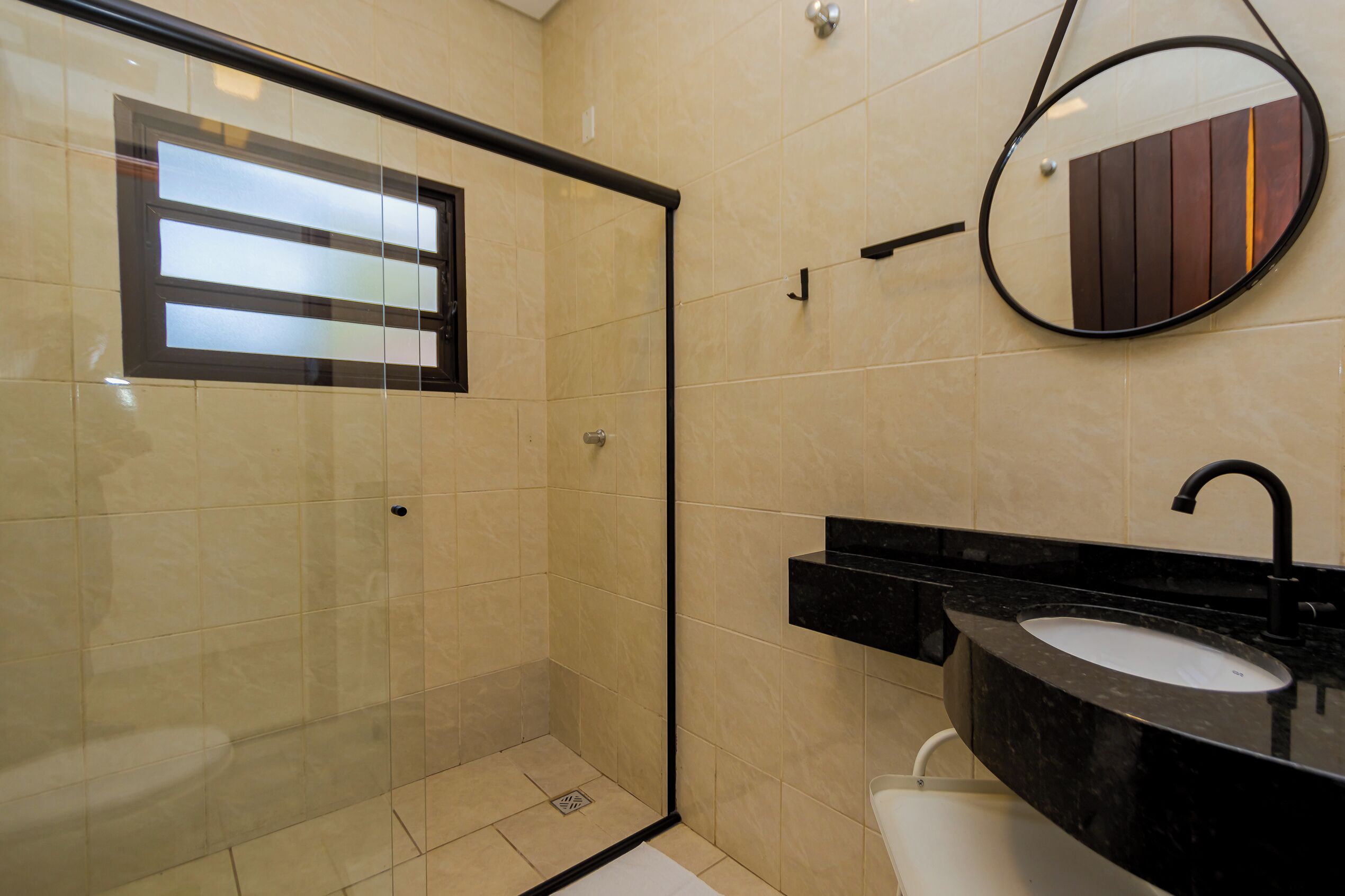 A modern bathroom with a glass-enclosed shower, a black sink, and a mirror with a wooden panel design.