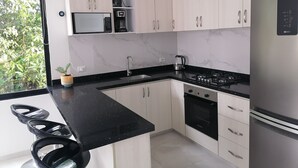 Una cocina moderna con gabinetes blancos, encimera negra, refrigerador de acero inoxidable, horno empotrado y estufa a gas.