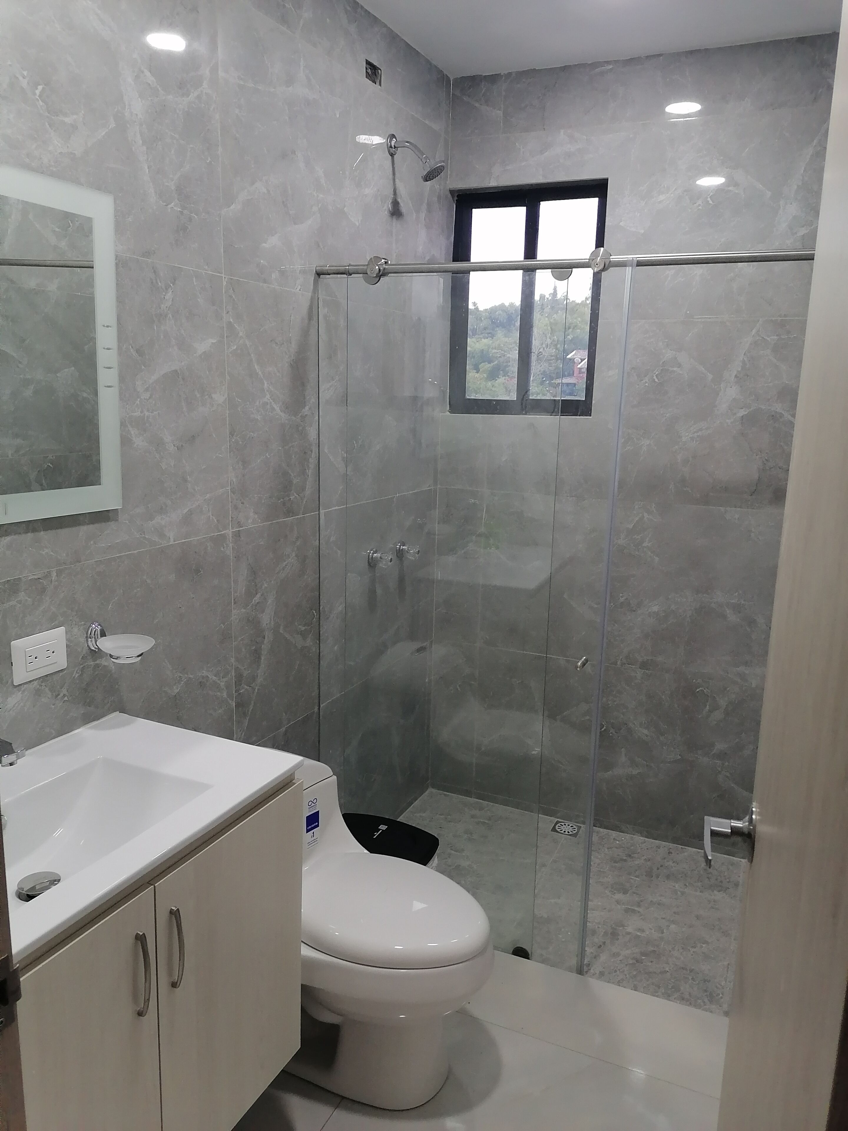 Un baño moderno con ducha envuelta en vidrio, inodoro blanco y lavamanos con espejo.
