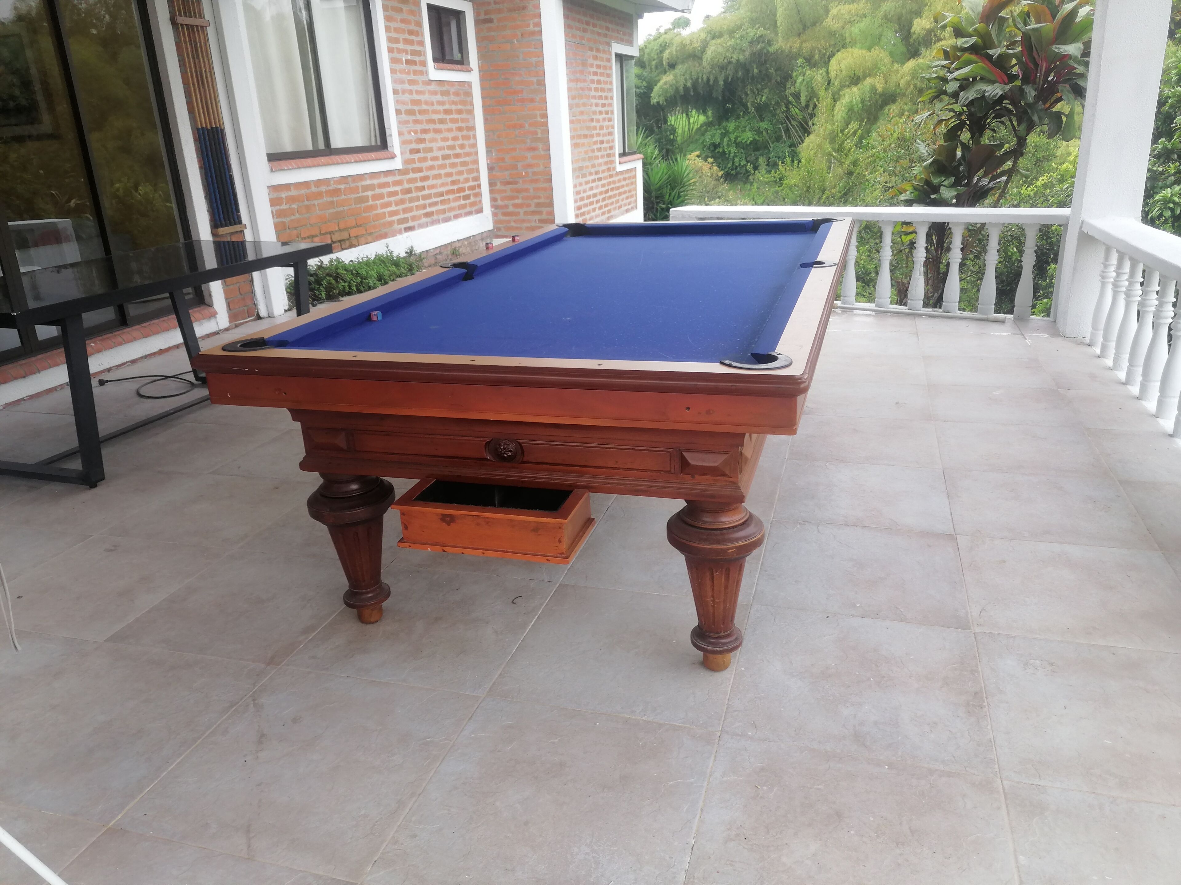 Een pooltafel op een terras met een bakstenen muur en beplanting op de achtergrond.