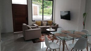 Una sala de estar moderna con un sofá, una mesa de comedor de vidrio con sillas y un televisor montado en la pared.