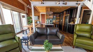 Una sala de estar acogedora con un sofá de cuero negro, dos sillones verdes y una mesa de centro de madera con una planta.
