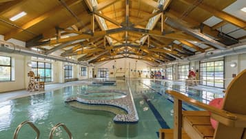 Una piscina interior con varias pistas, vigas de madera en el techo y grandes ventanales.