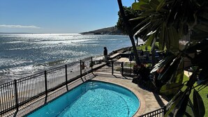 A swimming pool with a view of the ocean, surrounded by a fence and palm trees. - Cool 1BD Entire Condo On The Beach in Maalaea Harbor (Wailuku)