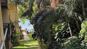 A narrow pathway flanked by lush greenery and a building with a balcony. - Cool 1BD Entire Condo On The Beach in Maalaea Harbor (Wailuku)