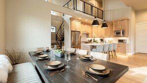 A modern kitchen with stainless steel appliances, a dining area with a dark wooden table set for six, and a staircase leading to an upper level. - New and Fun in Deer Valley East Village - Free Mountain Mover on demand ski shuttle (Heber City)