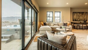 A spacious living room with a large sliding glass door, a leather sofa, a round coffee table, and a dining area with a high table and chairs. - New and Fun in Deer Valley East Village - Free Mountain Mover on demand ski shuttle (Heber City)