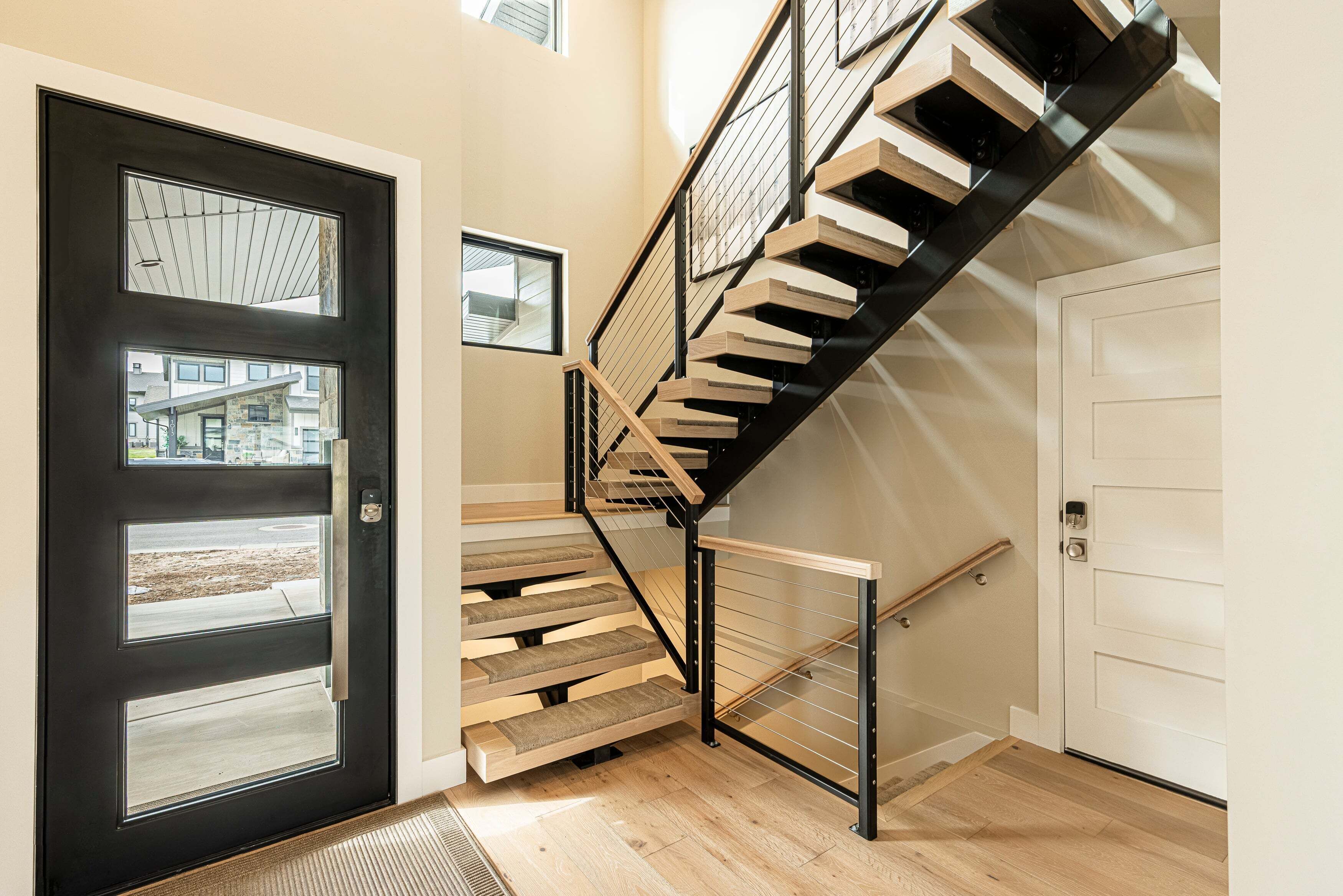 A modern staircase with wooden steps and black railings, leading to a white door.