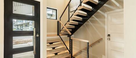A modern staircase with wooden steps and black railings, leading to a white door.