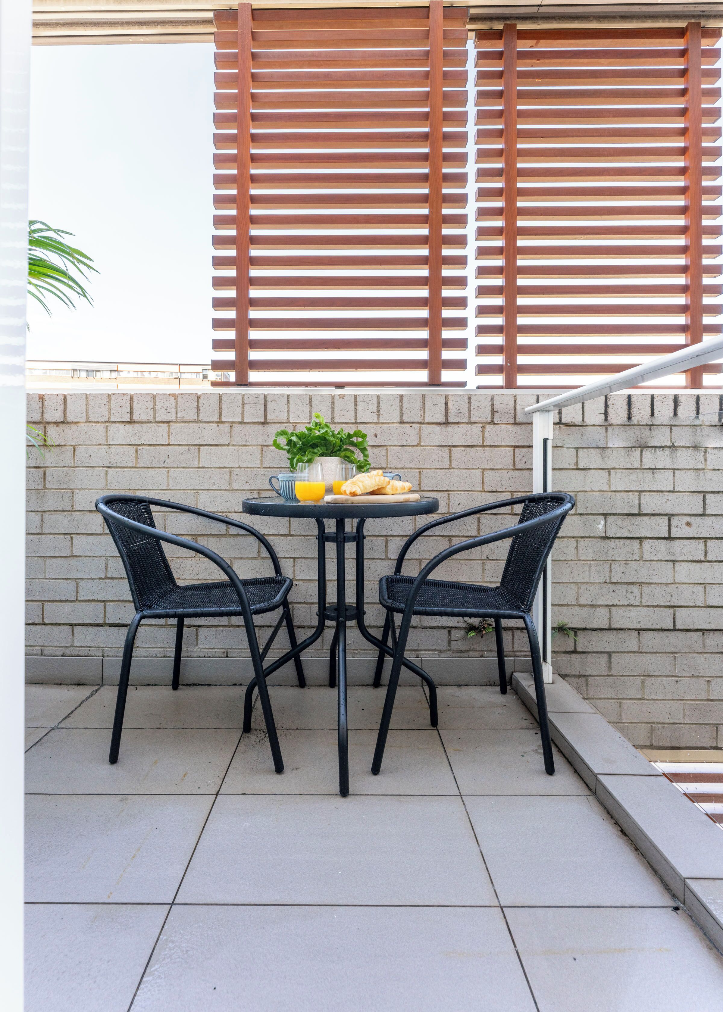 Une terrasse extérieure avec une table et deux chaises, un mur en briques et un plafond en bois à lattes.