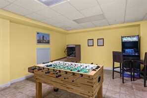 Een kamer met een tafelvoetbalspel, een televisie en een klein tafeltje met stoelen.