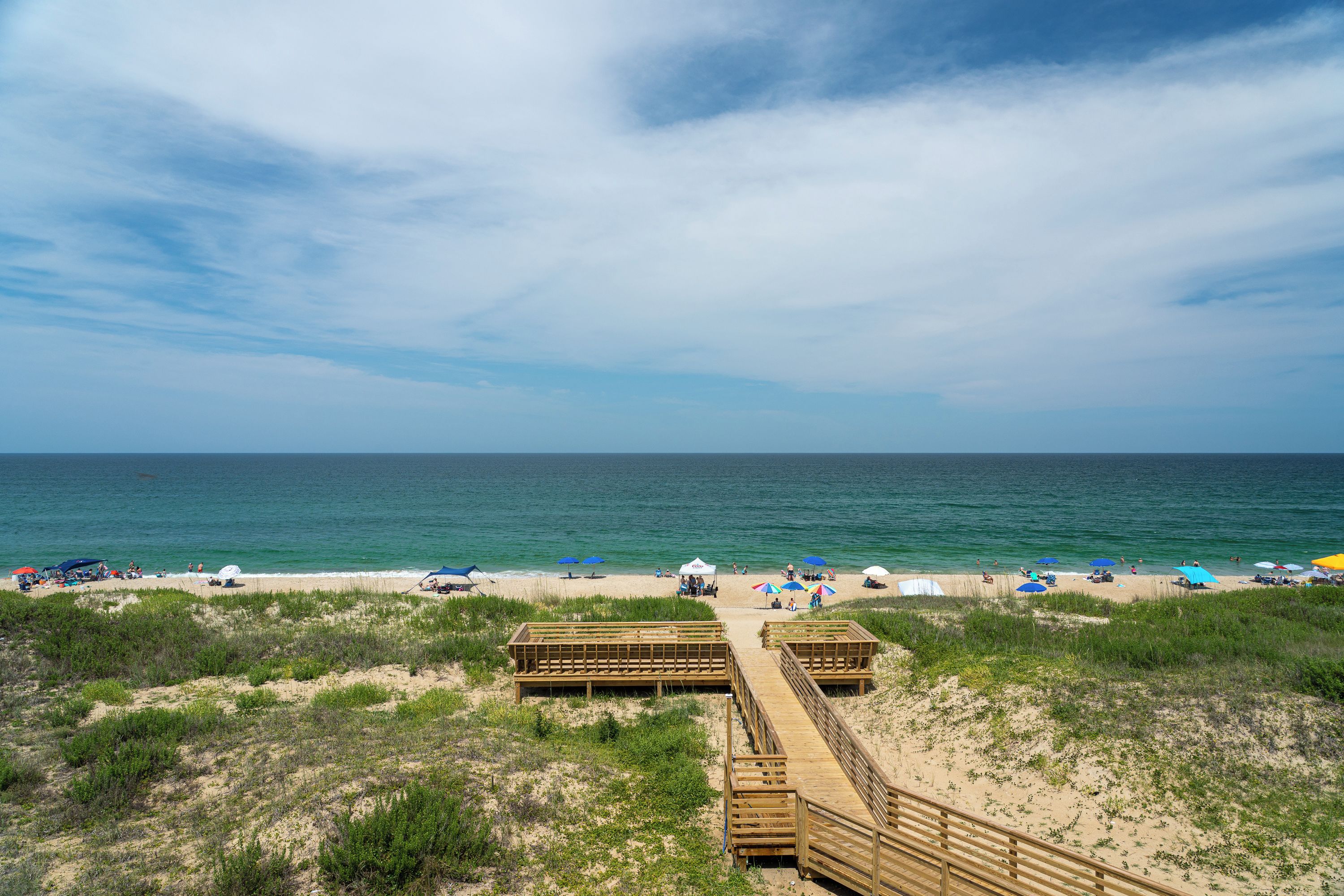 Ein Strand mit Holzstegen, Strandkörben und Menschen, die das Meer genießen.