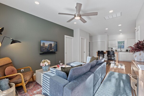 A modern living room with a grey sofa, a wooden chair, a coffee table, and a TV mounted on the wall.