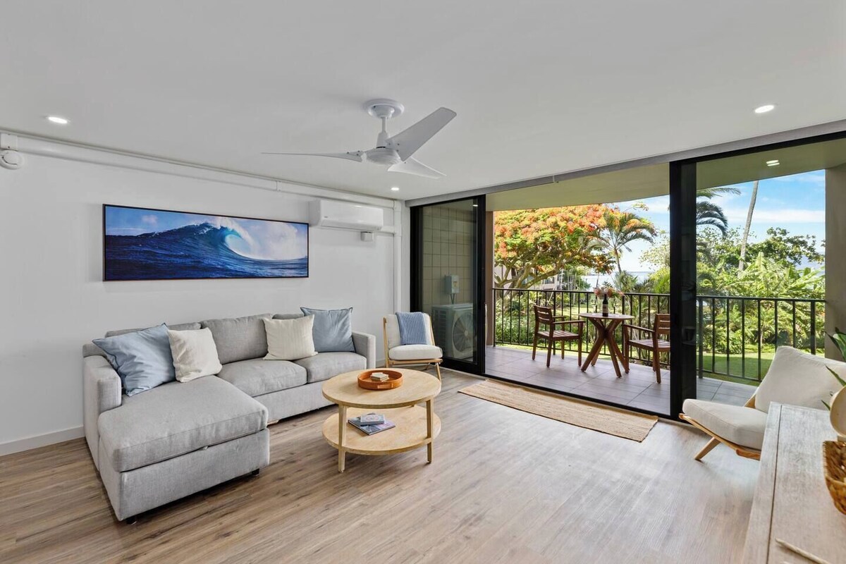 Una sala moderna con un sofá gris, una mesa de centro de madera y vistas a un balcón con mobiliario exterior.