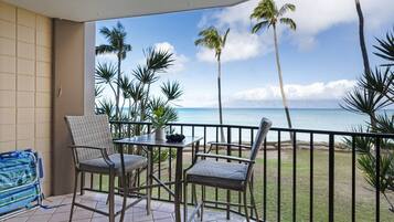 A balcony with two chairs and a small table, overlooking a beach with palm trees and the ocean.
