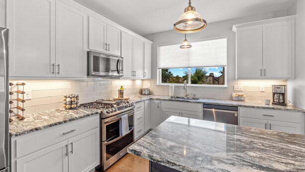 A modern kitchen with white cabinets, a stainless steel refrigerator, a built-in oven, a microwave, and a large island with a marble countertop. - Spacious 4BR w/ Garage Near SLU & Hospital | Park-Adjacent | STL (St. Louis)