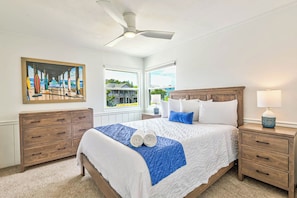 Relax in this serene bedroom with a large bed, nightstand, dresser, and ceiling fan, offering a peaceful view of the outdoors.