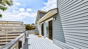 A wooden deck with a railing, a covered outdoor seating area, and a building with large windows. - Duck, Duck, Goose | 650 ft to the beach | Hot Tub (Duck)