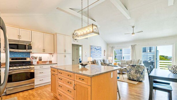 A spacious kitchen with wooden cabinets, a large island, and a dining area with a table and chairs. - Duck, Duck, Goose | 650 ft to the beach | Hot Tub (Duck)