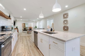 A modern kitchen with a central island, white cabinetry, and pendant lighting. - Sunset Over the Dunes by Carolina Getaway - Oceanfront POOL & HOT TUB OPEN (Carolina Beach)