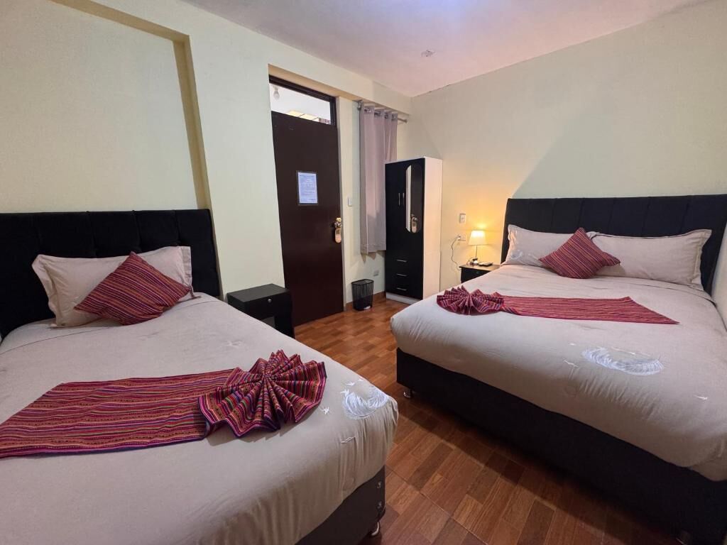 Two beds with striped blankets, a wooden floor, a door, and a nightstand with a lamp.