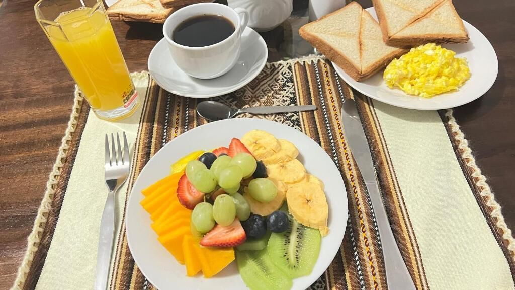 Uma mesa de café da manhã com uma travessa de frutas, torradas, ovos mexidos e um copo de suco de laranja.