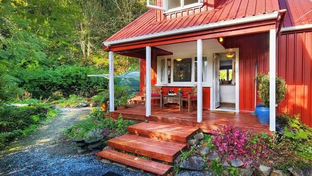 A red wooden house with a porch, a dining table, and a garden.
