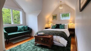 A cozy bedroom with a bed, a green sofa, a wooden chest, and two bedside lamps.