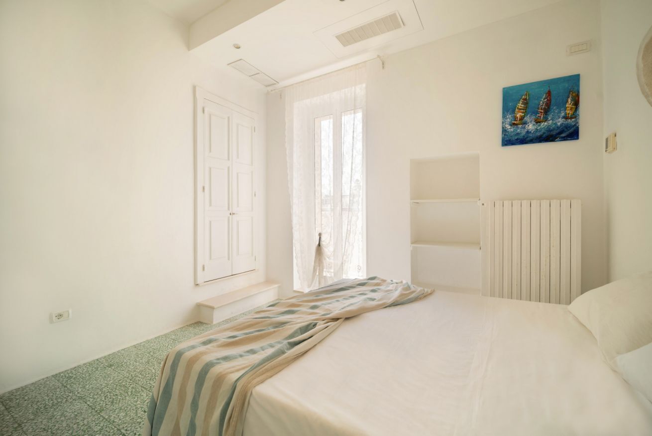 A bedroom with a bed, a window with curtains, a radiator, and a painting on the wall.