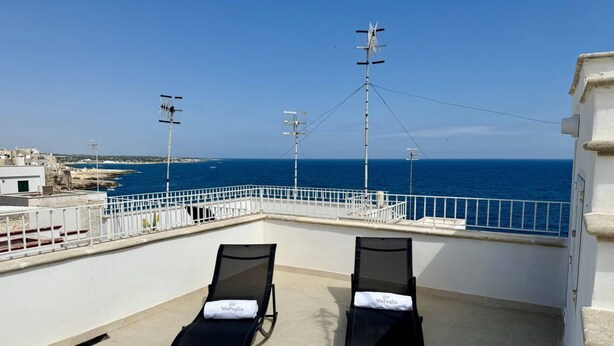 A rooftop terrace with two sun loungers, a railing, and a view of the sea.