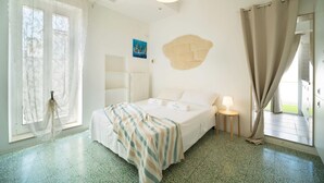 A hotel room with a bed, a bedside table with a lamp, a window with curtains, and a wall-mounted artwork.