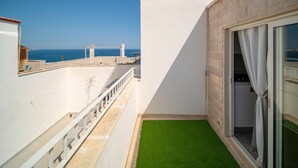 A balcony with a view of the sea, a glass door, and a small artificial grass area.