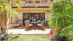 A patio with a table and chairs, surrounded by palm trees and a view of a building. - Charming 1-bedroom condo in lovely Kihei with WiFi, AC (Kihei)