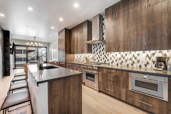 A modern kitchen with wooden cabinets, a large island, stainless steel appliances, and a geometric backsplash.