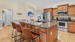 Eine Küche mit Holzausstattung, Granit Arbeitsplatten, Edelstahlgeräten und einer Bar mit Hockern.