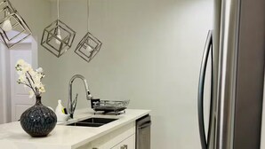 A modern kitchen with a stainless steel refrigerator, a white countertop, a sink, and a dish rack. - Luxury 3 Bedroom Home | Fireplace | 84” Pool Table| Air Conditioning| Garage (Edmonton)