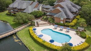 Un complexe hôtelier doté d’une grande piscine entourée de chaises longues et de parasols, d’une terrasse en bois et offrant une vue sur le lac.