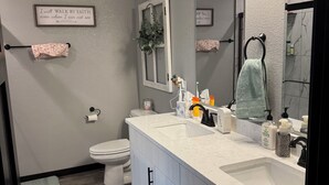 Une salle de bain moderne avec un meuble-lavabo blanc, un grand miroir et un espace douche.