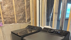 Une pièce contenant deux appareils électroménagers noirs, peut-être des machines à laver, et une poubelle.