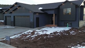 Une maison moderne à deux étages, dotée d’un garage, d’un porche abrité et d’une pelouse bien entretenue, parsemée de quelques plaques de neige.