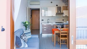 A modern kitchen with a dining area, a sofa with patterned cushions, and a wooden door. - Elegant two-bedroom apartment with air conditioning and a large balcony overlooking the lake. Guests can relax in the shared swimming pool, immersed in a peaceful atmosphere. Perfect for a comfortable and unforgettable stay.The apartment is located on th (Bellano)