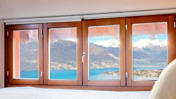 A hotel room with a large bed, wooden sliding doors, and a view of mountains and a lake. - Elegant two-bedroom apartment with air conditioning and a large balcony overlooking the lake. Guests can relax in the shared swimming pool, immersed in a peaceful atmosphere. Perfect for a comfortable and unforgettable stay.The apartment is located on th (Bellano)