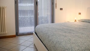 A bedroom with a bed, a radiator, a sliding glass door, and a nightstand with a lamp. - Discover the pleasure of living in the heart of Bellano, kissed by the beauty of Lake Como.Its central location allows you to immerse yourself in the vibrant life of Bellano, with its characteristic shops, delicious restaurants and authentic atmosphere.  (Bellano)