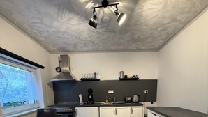 Ett kompakt kök med matplats, inrett i modern stil med ljusa trägolv, vita skåp och en svart bänkskiva.