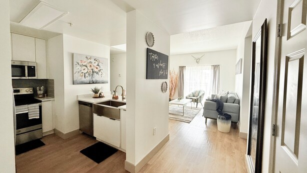 A modern kitchen with a microwave, stove, and sink, a dining area with a table and chairs, and a living room with a sofa and a coffee table.