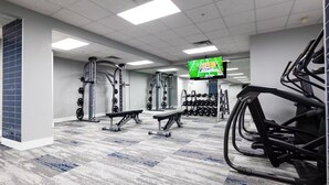 A gym with weightlifting equipment, treadmills, and a TV screen.
