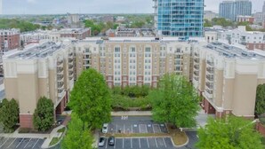 A multi-story residential building with a central courtyard, parking area, and surrounding greenery.