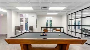 A pool table in a room with white walls, a large window, and a door.
